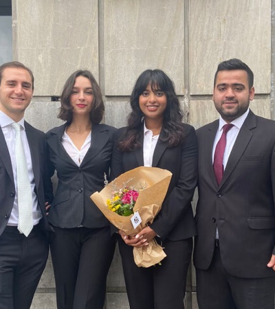 Four professionals in business attire, with one holding a bouquet of flowers, standing in front of a building.