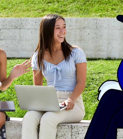 A group of young people sitting outside on steps, interacting with each other and a laptop, with a cartoon character digitally added to the scene.