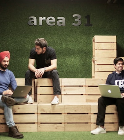 Five people having a casual meeting on wooden bleachers in a creative office space labeled 'area 31'.