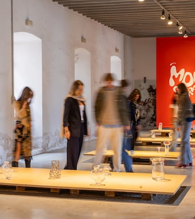 People viewing an art exhibition in a gallery with red and white walls and modern artwork installations.
