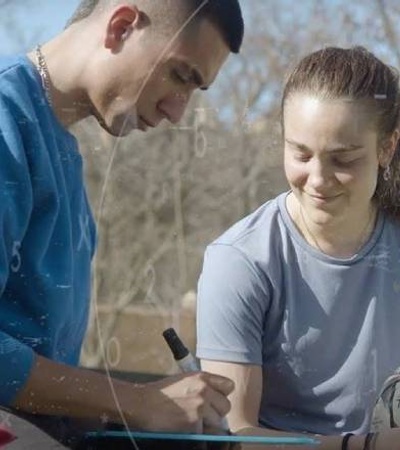 A young man autographing a soccer ball for a smiling young woman in an outdoor setting