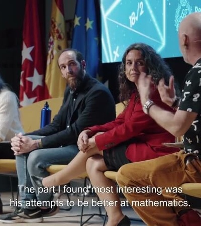 Four people participating in a panel discussion with an audience, where one man is gesturing while speaking.