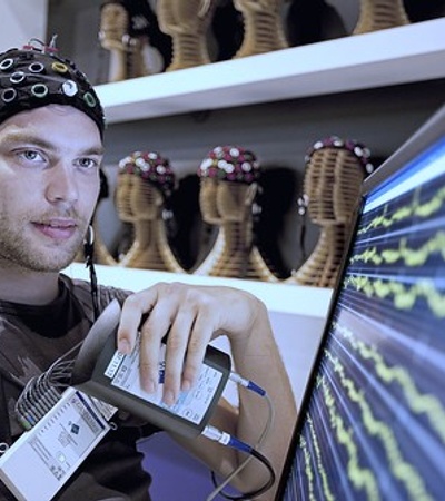 A man wearing an EEG cap observes brainwave readings on a monitor.