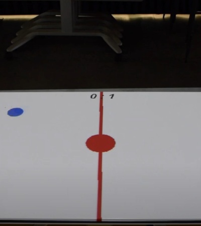 Two players are engaged in a game on a projected table with a red and blue disk.