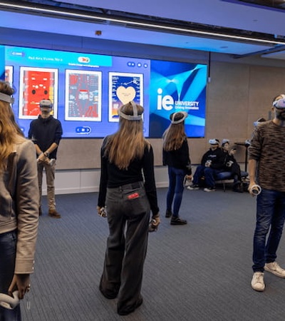 People using virtual reality headsets in a room with a large digital screen displaying various interactive options.