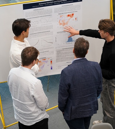 A group of young adults is discussing research findings presented on a poster at a conference.