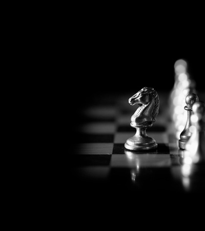 A close-up of a silver knight chess piece on a dark chessboard.
