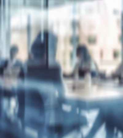 A blurred image of people in a business meeting in an office environment.