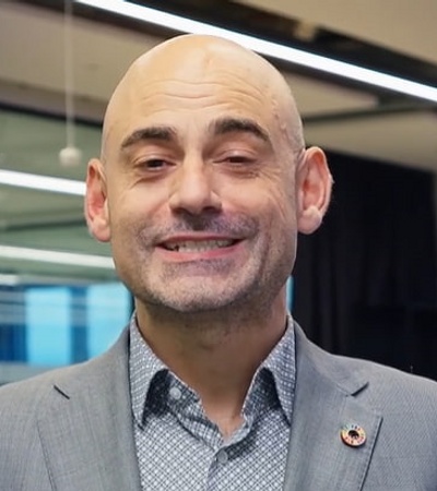 A bald man in a suit smiles in an office environment.