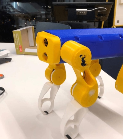 A toy robot with yellow legs and a blue body on a desk.