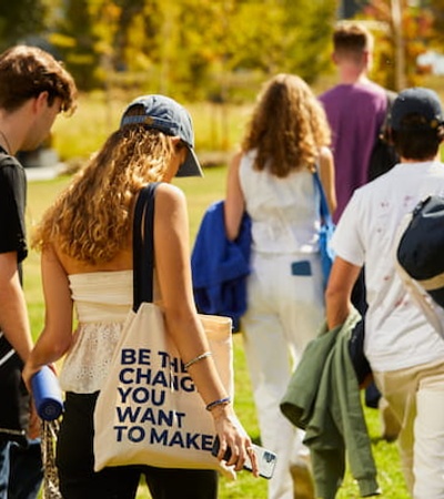 A group of young people walking in a park, one carrying a bag with a motivational message.