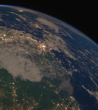 A view of Earth from space showing part of a continent illuminated by city lights under a dusky sky.