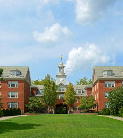 A picturesque view of buildings and a clock tower framed by greenery under a blue sky.