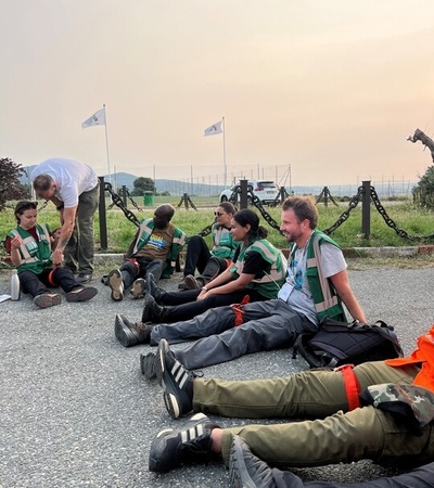 A group of people wearing green vests sit on the ground in a training or outdoor setting.