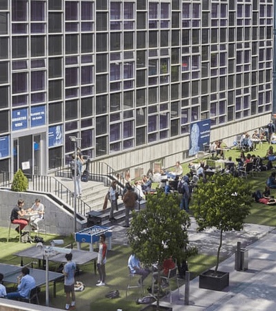 A lively outdoor scene with people socializing and working in front of a modern building.