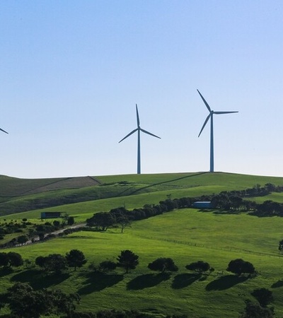 Three wind turbines stand on green hills under a clear blue sky.