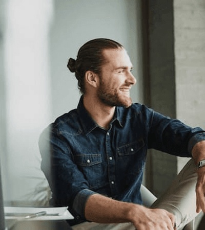 A man with a man bun smiling and looking away from the camera in a modern office setting.