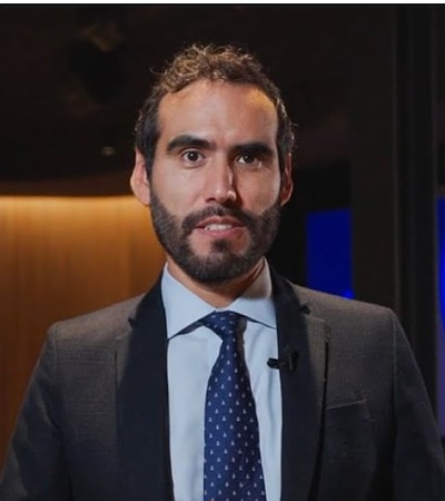 A man in a suit stands in front of a digital screen displaying graphic designs.