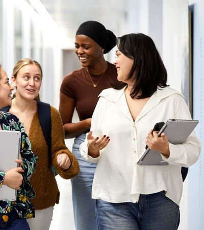 A group of four young women are walking and chatting together in a hallway.