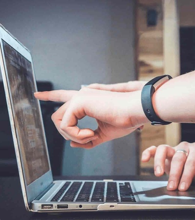 A person pointing at a laptop screen while another person watches.