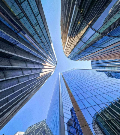 A dynamic upward view of towering skyscrapers converging into a clear blue sky.