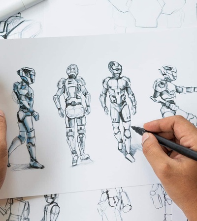 A person sketches various poses of robotic characters on paper, surrounded by additional character sketches and design iterations.