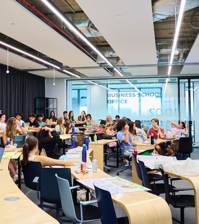 A classroom filled with students listening to a teacher presenting.