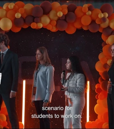 Four people standing on a stage, decorated with orange balloons and lights, appearing to be engaged in a presentation