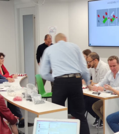 A group of people sitting around a table in a meeting room, discussing over documents with a presentation in the background.