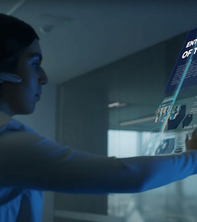 A woman interacts with a futuristic holographic display containing various business analytics and profiles.