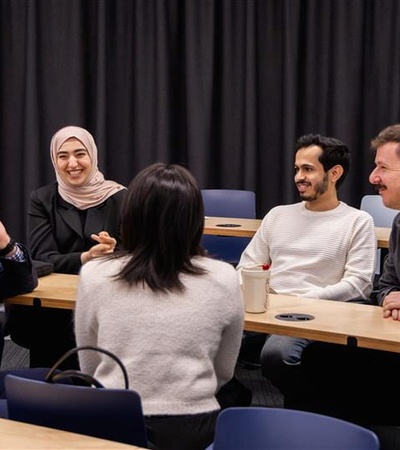 A group of five people engaged in a discussion at a table in a classroom setting.