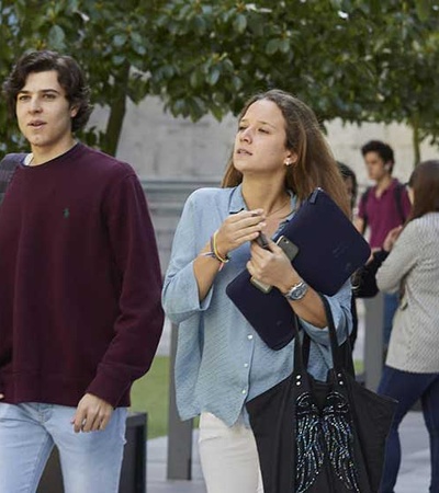 A group of young adults walking on a college campus, some engaged in conversation and others looking ahead.