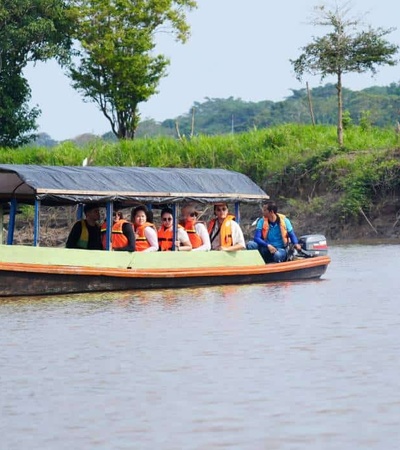 A group of people wearing life jackets traveling by boat on a river with lush greenery in the background.