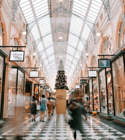 A bustling shopping arcade adorned with holiday decorations and a central Christmas tree.