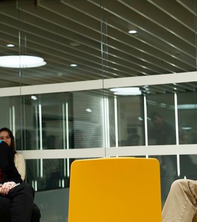 A man and a woman sitting in a modern office space, talking.