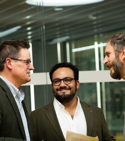 Three men in a business setting, casually interacting and smiling.