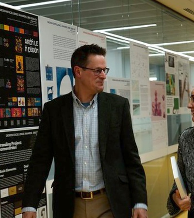 Two people, a man and a woman, walking and talking in a corridor with informational posters on the walls.