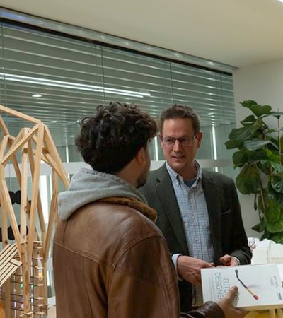 Three people discuss a model bridge in an office environment.