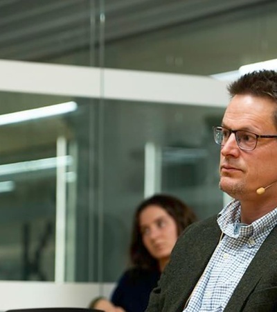 A man wearing glasses and a gray blazer attends a meeting in a modern office setting.