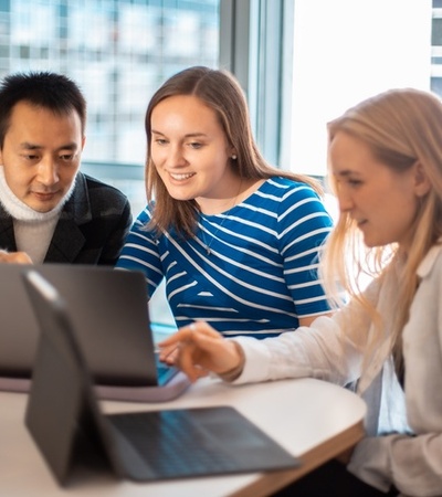 Three individuals are collaborating on laptops at a bright, modern workspace.