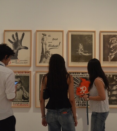 A group of people examining various framed artworks displayed on a gallery wall.