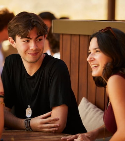 A young man and two women smiling and talking at a cafe table.