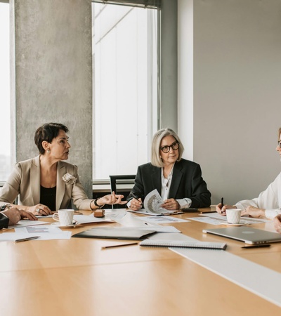 A group of five professionals in a meeting around a table in a modern office setting.