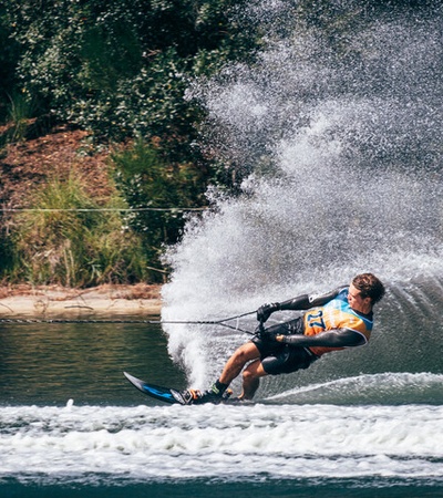 A person waterskiing on a lake, creating a large spray of water.