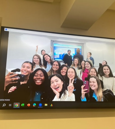 A group of people smiling and posing cheerfully for a virtual meeting displayed on a large monitor.