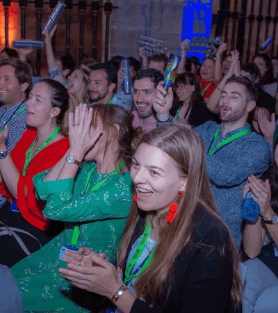 A group of people clapping and smiling during an event indoors, illuminated by blue lighting.