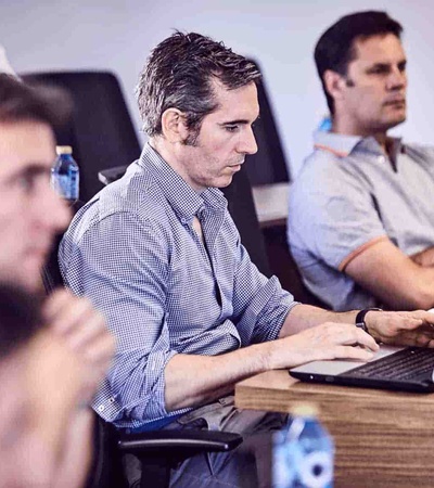 A group of men focused on laptops and listening during a business meeting in a modern office.