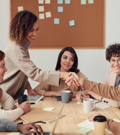 five people sat on a table, and two of them are shaking hands in what it seems to be two people presenting for each other for the first time