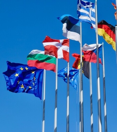 A collection of flags from various countries waving against a clear blue sky.