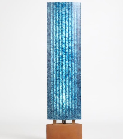 A tall blue sculptural artwork on a brown pedestal against a white background.